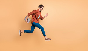 Full length body size view of his he nice attractive cheerful cheery successful brunet guy jumping in air carrying laptop running fast late hurry-up isolated over beige color pastel background